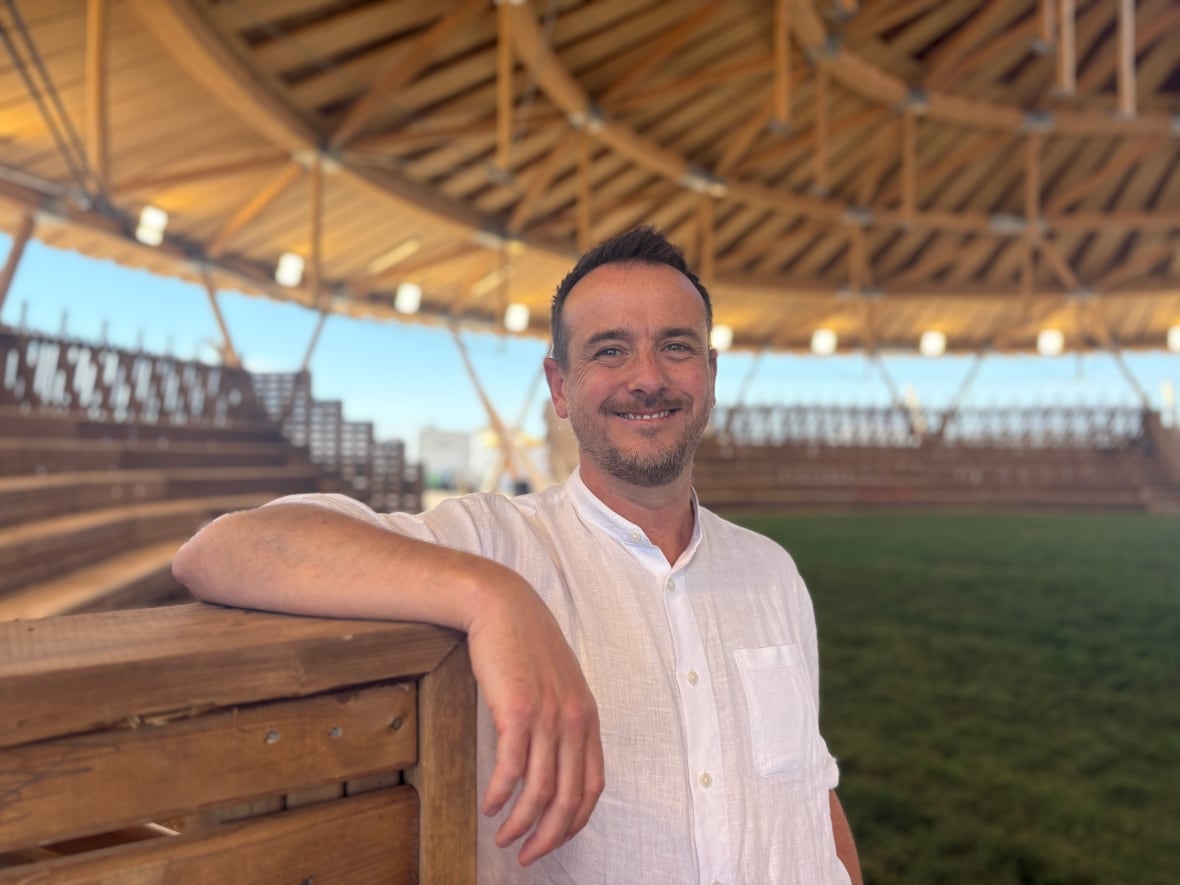 A man leans over a wooden edge wile posed under a wooden arbour.
