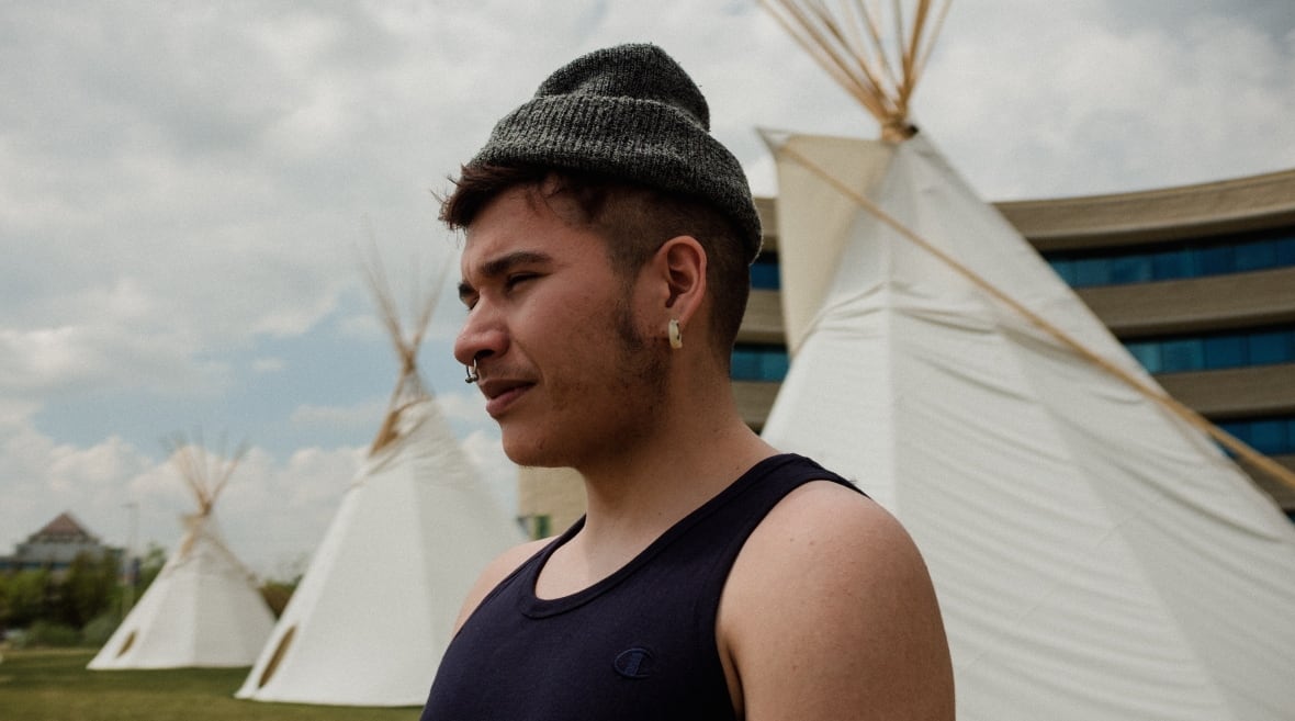 a man looks into the distance. there are teepees behind him