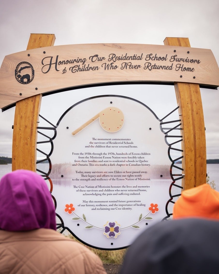 Shiishiikun, a traditional rattle, along with inscription of the impacts of residential schools written on the memorial plaque.